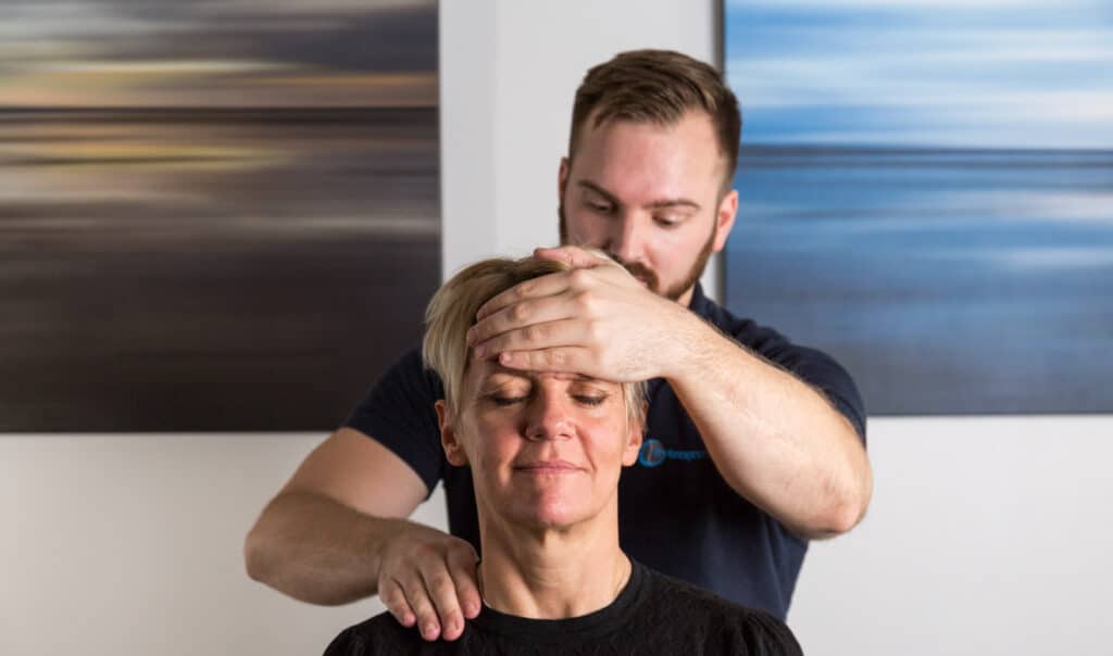 En Naprapat stöttar patientens panna med sin ena hand och pressar med den andra bakom patientens axel